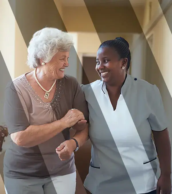 Smiling home caregiver and senior woman walking together through a corridor.