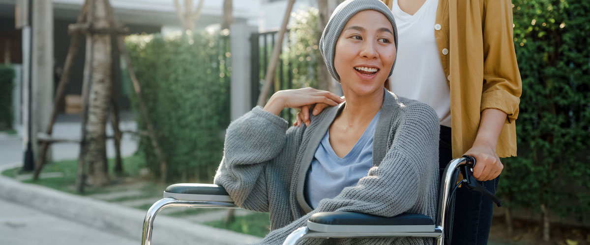 Young Asian cancer patient sitting in wheelchair outside their home.