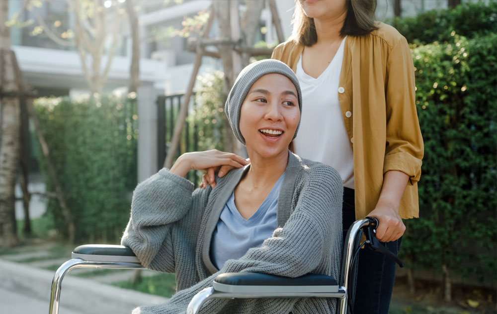Young Asian cancer patient sitting in wheelchair outside their home.