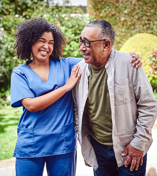 Smiling home caregiver and senior woman walking together through a corridor.